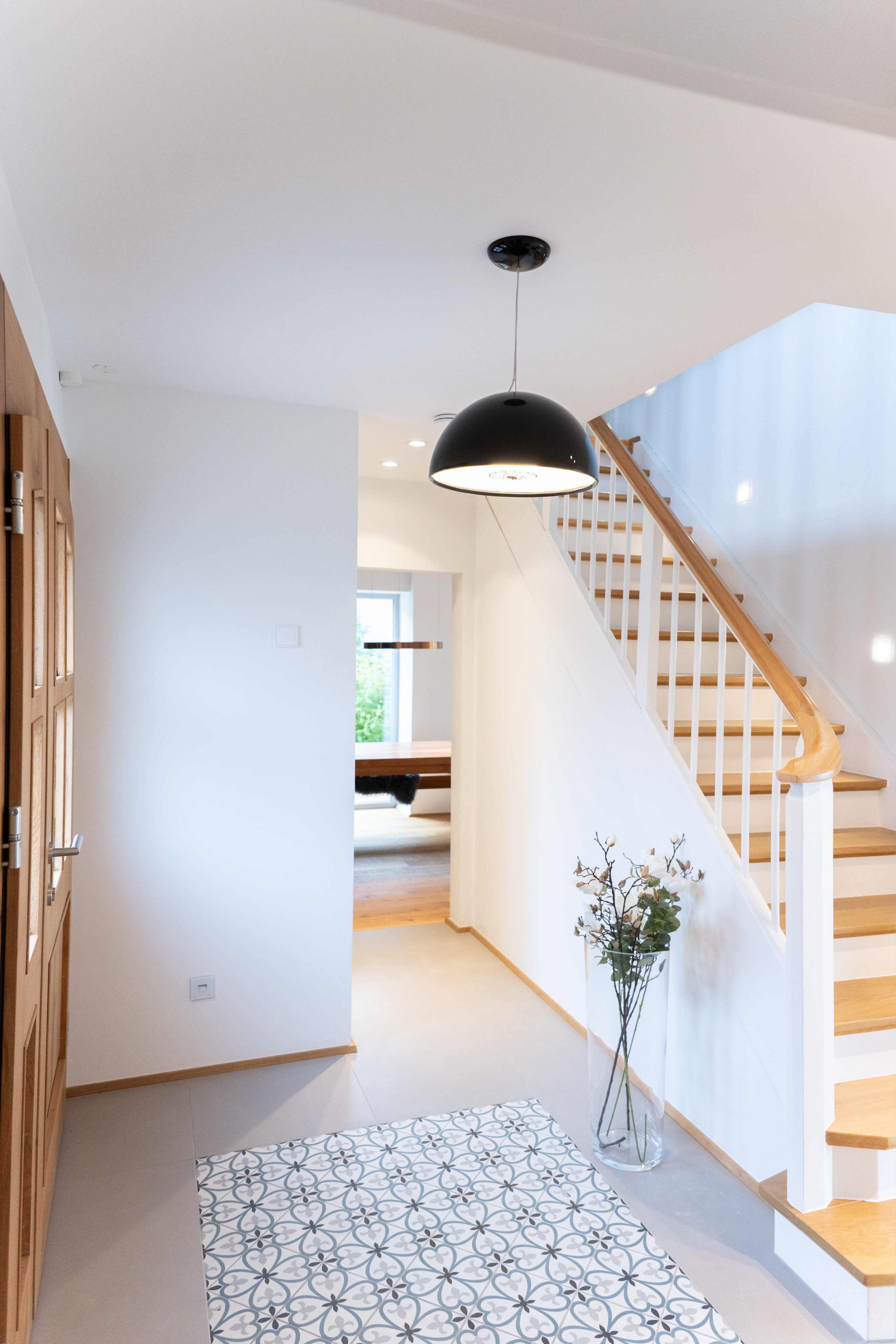 Heller Eingangsbereich mit skulpturaler Treppe und markanter Pendelleuchte.