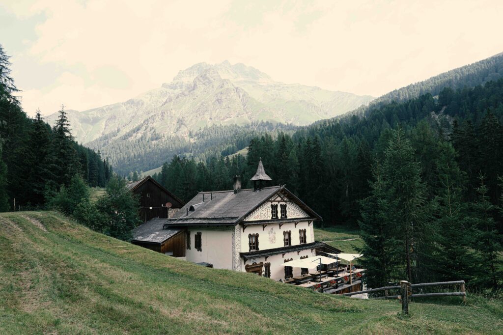 Traditionelles alpenländisches Gasthaus mit weißer Fassade und Verzierungen vor einer beeindruckenden Bergkulisse und dichtem Nadelwald.
