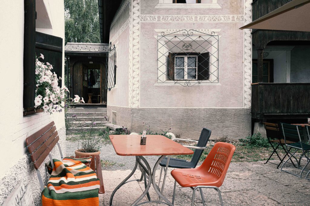Rustikale Terrasse vor einem historischen Gebäude mit verzierten Fassaden, Holzbalkon und gemütlicher Bestuhlung in einer exklusiven Umgebung.